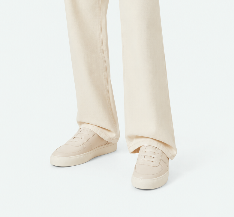 A model wearing off-white wide-leg jeans, a cream short-sleeve knit top, and cream sneakers, photographed against a clean white studio background.