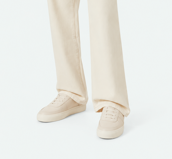 A model wearing off-white wide-leg jeans, a cream short-sleeve knit top, and cream sneakers, photographed against a clean white studio background.